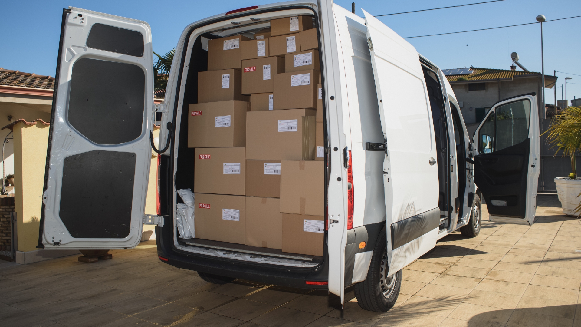 A white delivery van with its doors open, loaded with cardboard boxes 